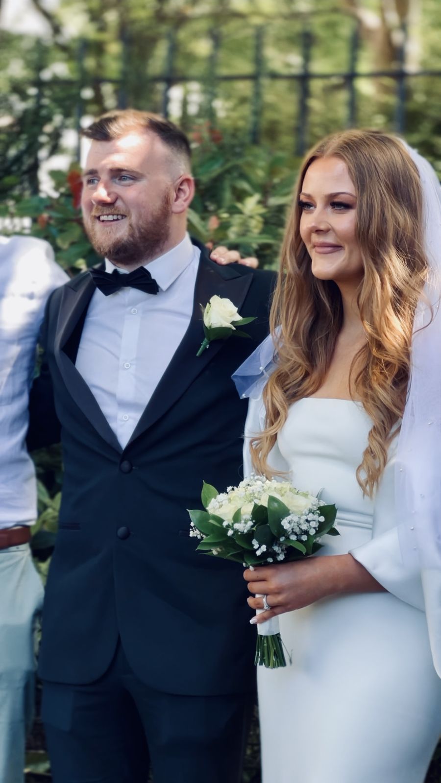 Groom and bride smiling side by side, bride holding white roses